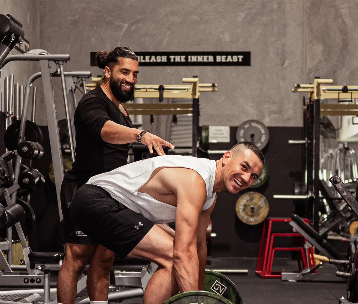 A Kaos Fitness coach guiding a member through a barbell row on the training floor